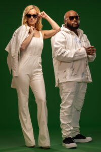 blonde woman in white jumpsuit leaning on man in white hoodie against green background