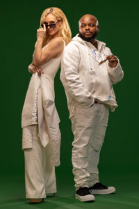 blonde woman lifting down sunglasses and man holding his own pair of sunglasses against green background