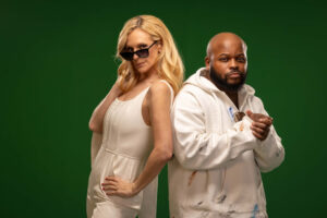 blonde woman in white outfit and man in street hoodie with sunglasses posing back-to-back together