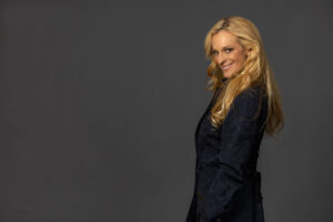 blonde woman smiling from side pose against grey background