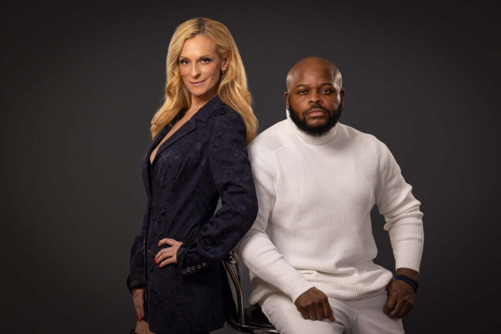 woman standing and man sitting in bar stool inside of a photo studio against a grey background