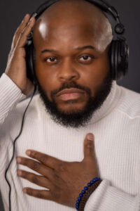 man with headphones and white turtleneck touching his chest