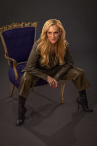 consuelo vanderbilt costin wearing a green outfit and sitting in a purple chair with a serious expression