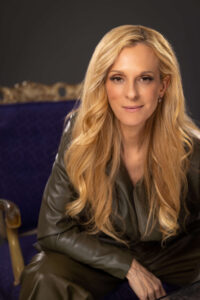 blonde woman sitting in purple chair with light smirk expression