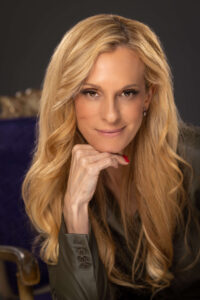 blonde woman smiling with hand under chin and purple chair in background