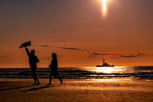 young boy and girl playing on beach with a kite during sunrise with boat in distance