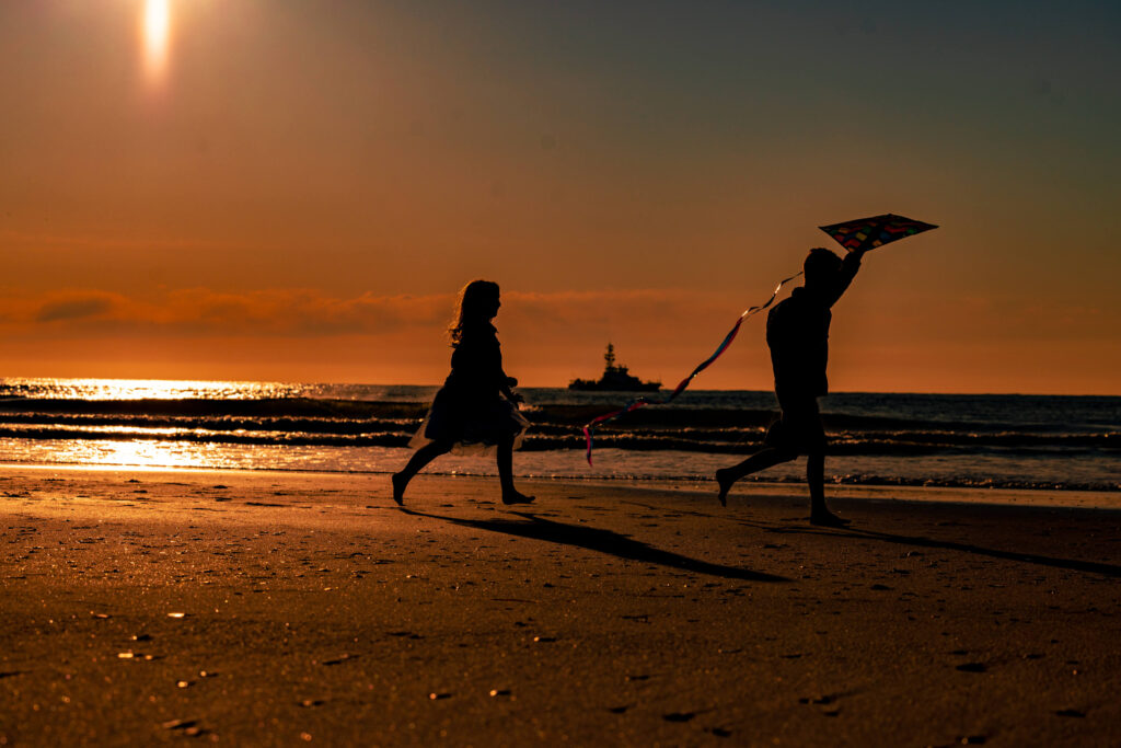 two children running on beach with kite during sunrise in Atlantic City New Jersey with boat
