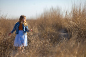 young girl walking in a sandy field with brown bushes