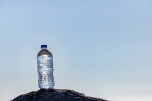 water bottle with blue cap sitting on a rock beneath clear sky