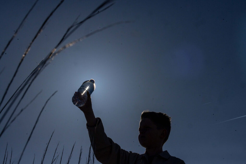 silhouette of young boy holding water bottle in air