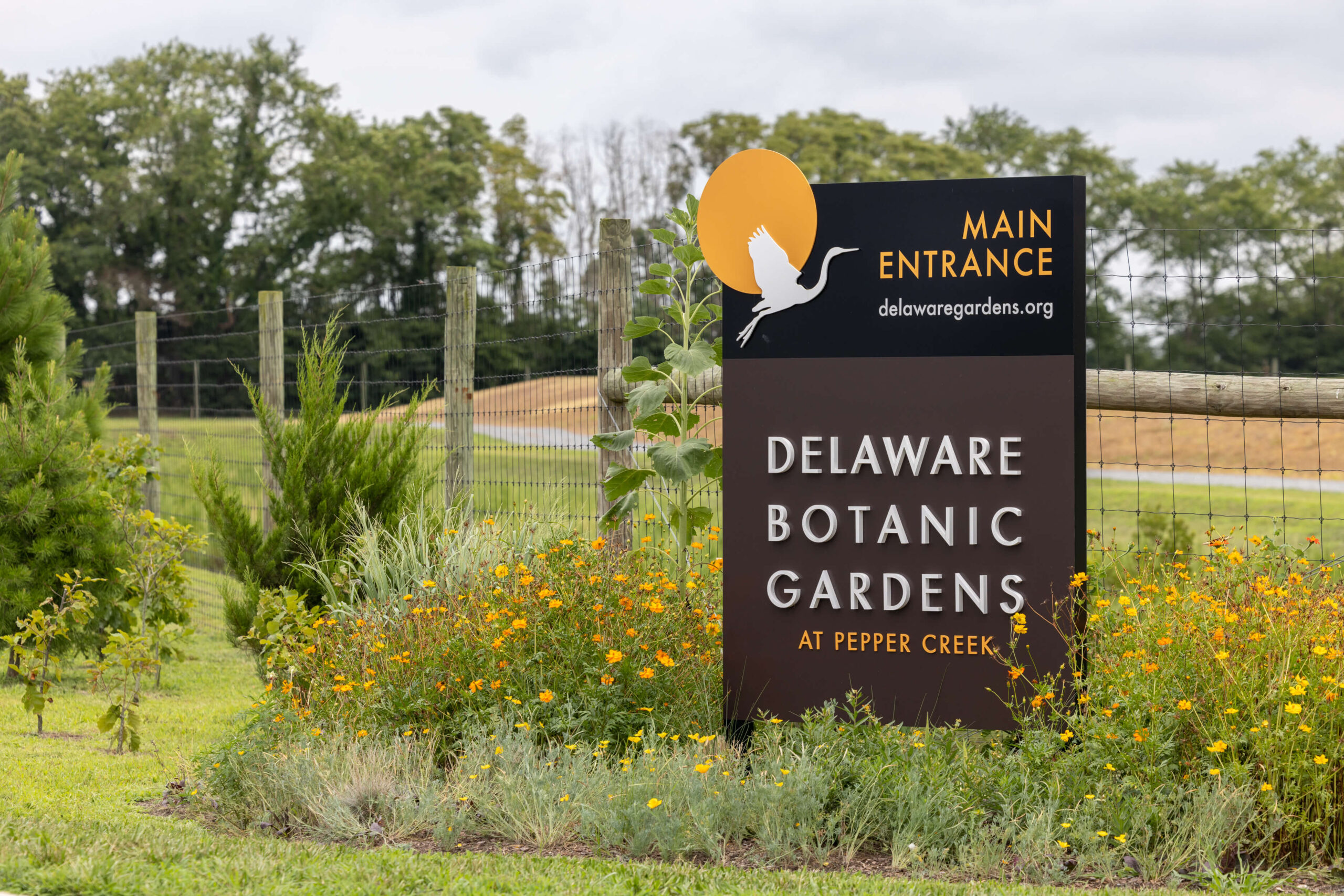 modern front entrance sign of the delaware botanic gardens at pepper creek with orange and yellow flowers