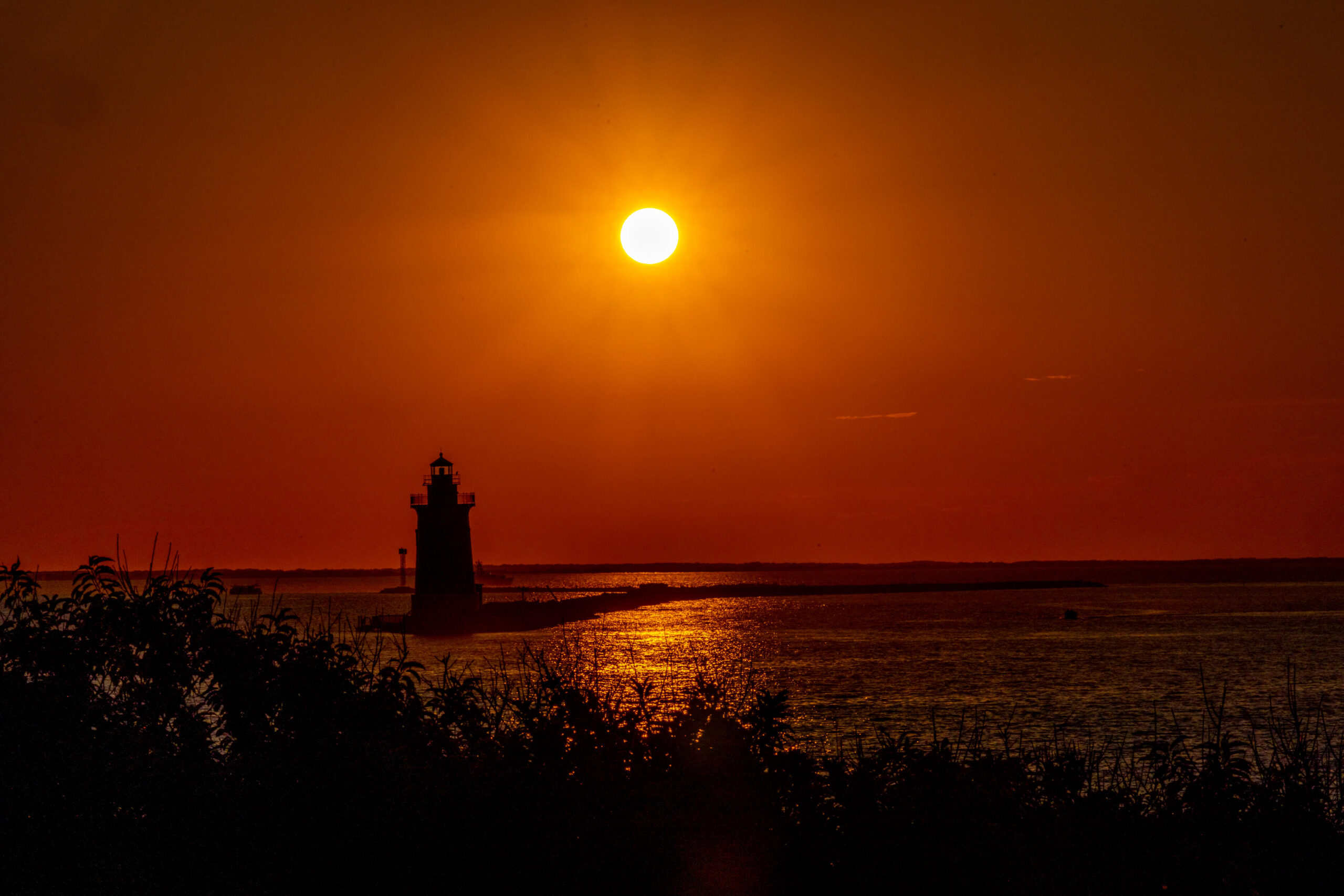dramatic golden sunset with orange sky and a silhouette of lighthouse in a bay