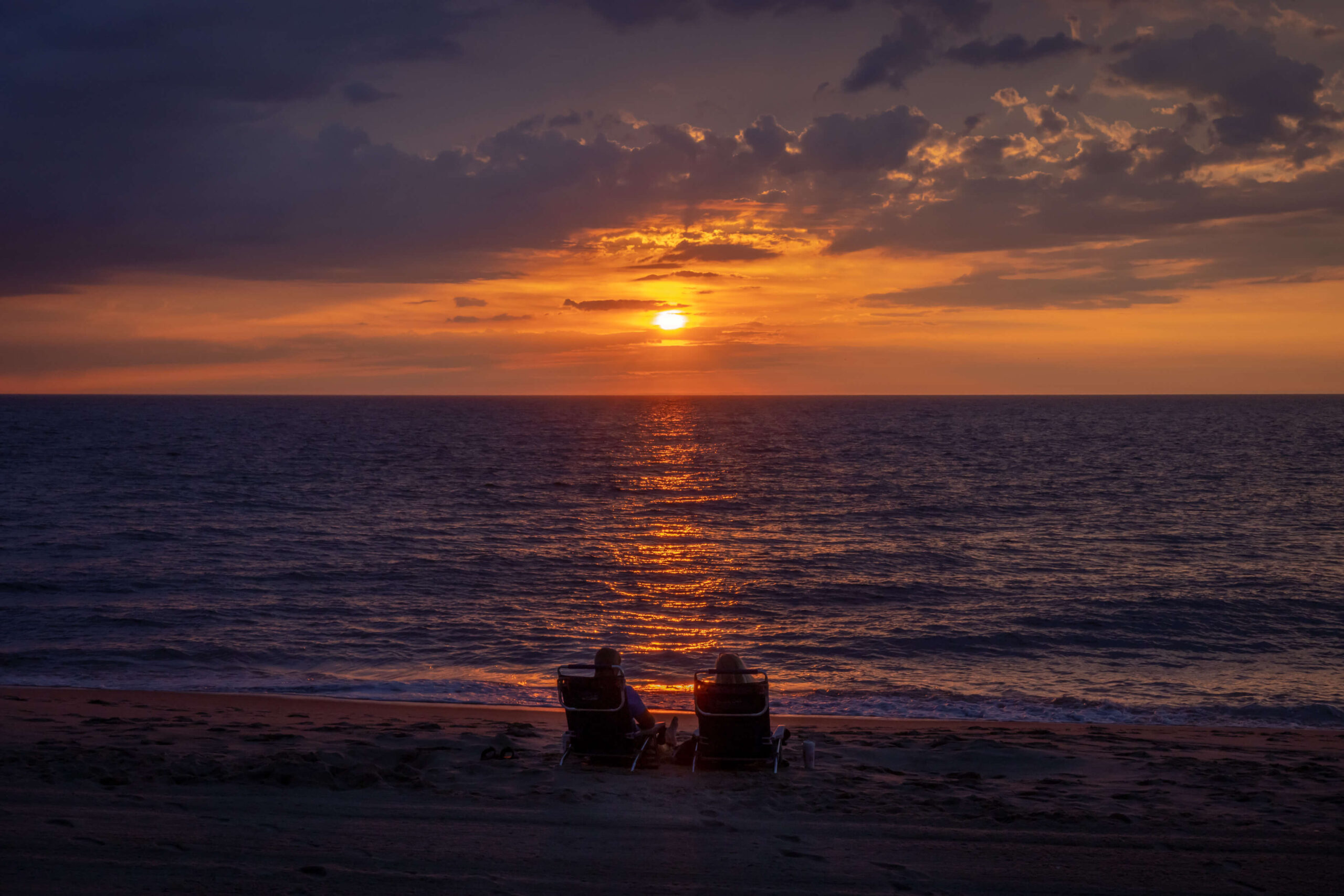 golden sunrise at rehoboth beach in Delaware with two silhouettes of people sitting in beach chairs