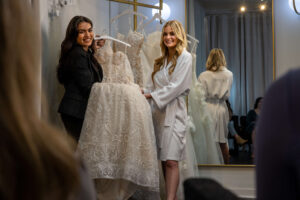 bride and stylist hold a wedding dress together and present it to family in changing room