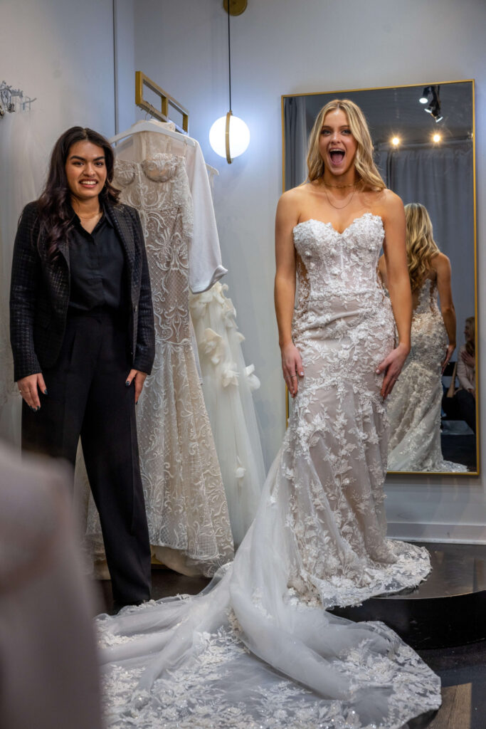 bride to be reacts to wedding dress with stylist in a changing room
