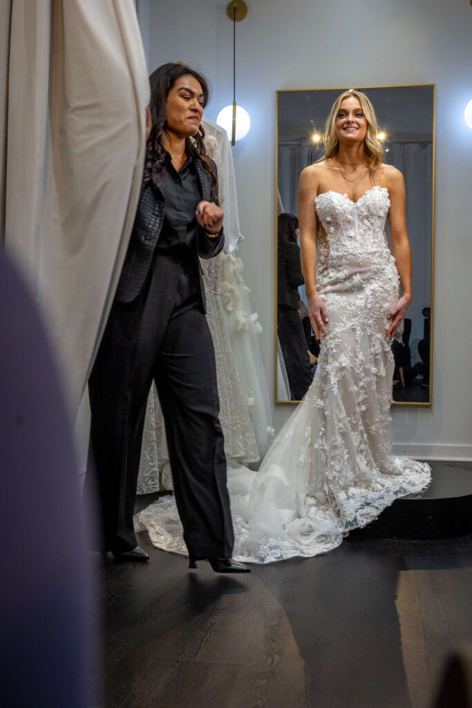 bridal salon stylist pulls changing room curtain for customer in wedding dress