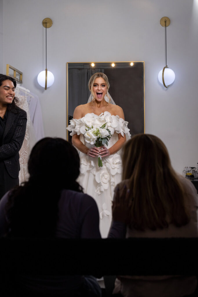 bride-to-be smiles at family and friends after revealing a wedding dress in a changing room at bridal salon
