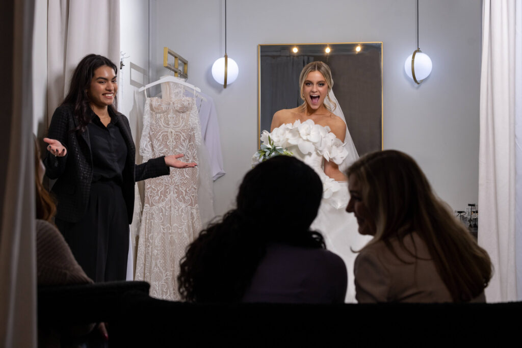 bride reveals wedding dress to family and friends from behind a dressing room curtain