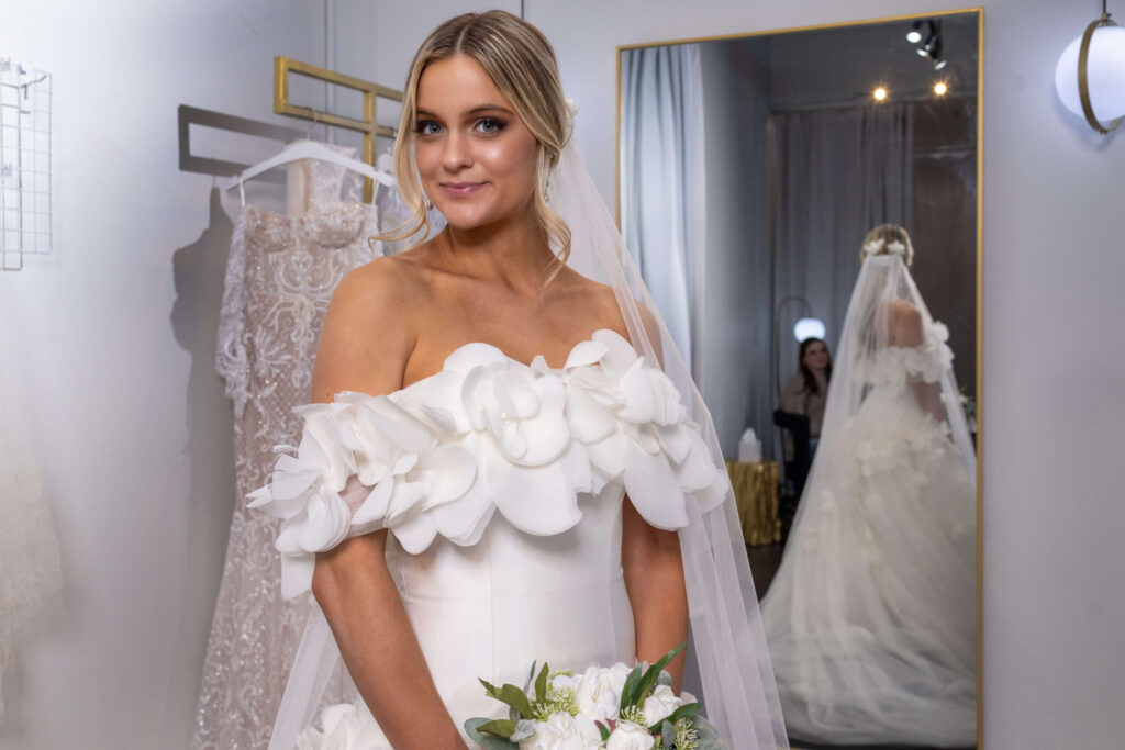 blonde woman smiling lightly in a elegant wedding dress with white flowers