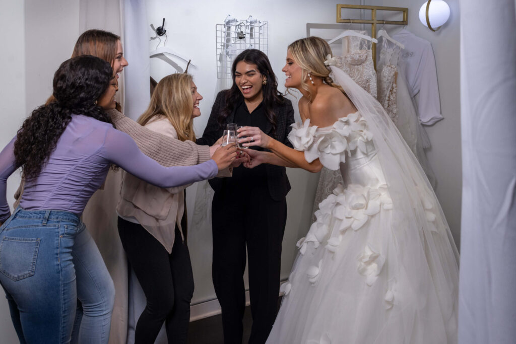 bride-to-be and friends touch champagne glasses and laugh together in a bridal salon