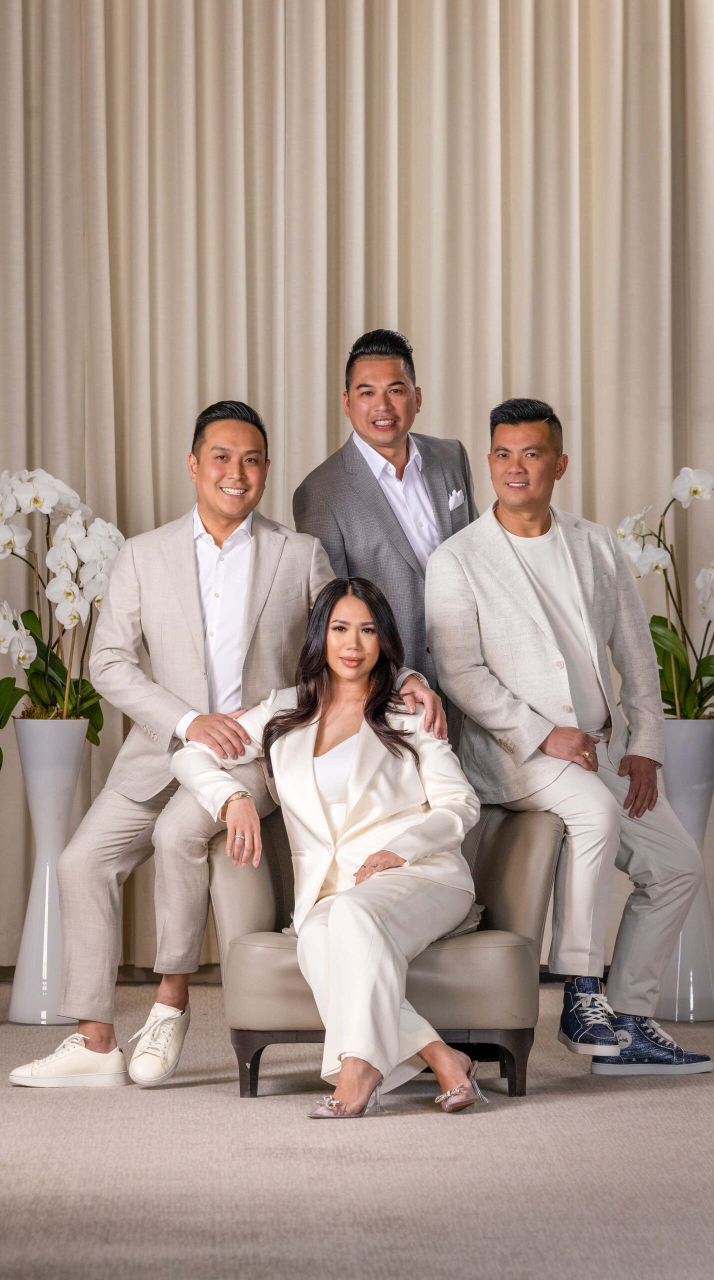 men and woman in light suits with beige drape background and orchid flowers