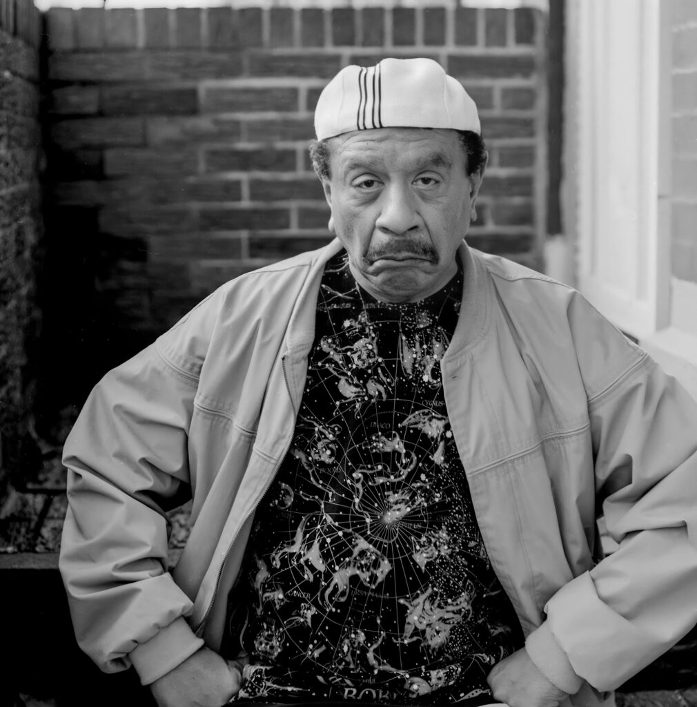 sherman hemsley with funny facial expression against brick wall