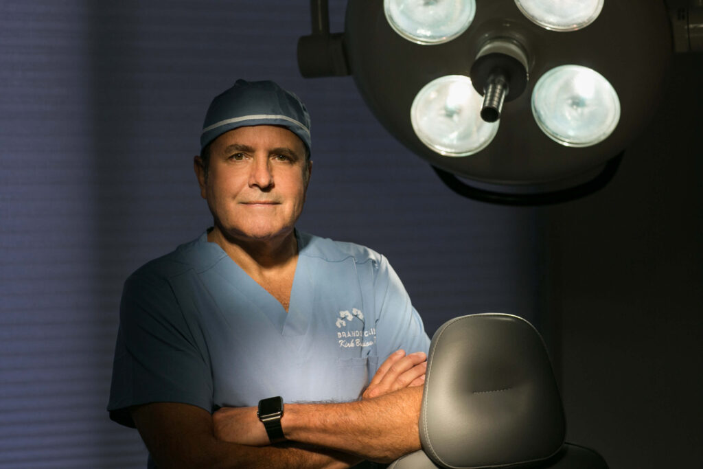 man wearing blue scrubs under an operating light and crossing his arms
