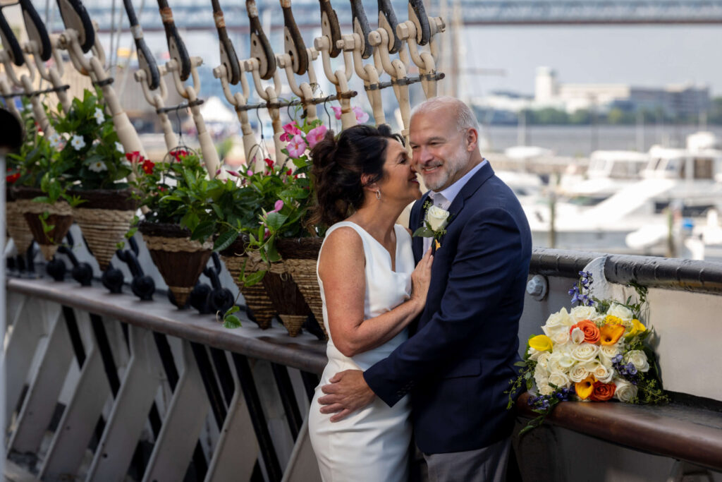 bride whispering to groom at the moshulu in philadelphia with flower bouquet on a table