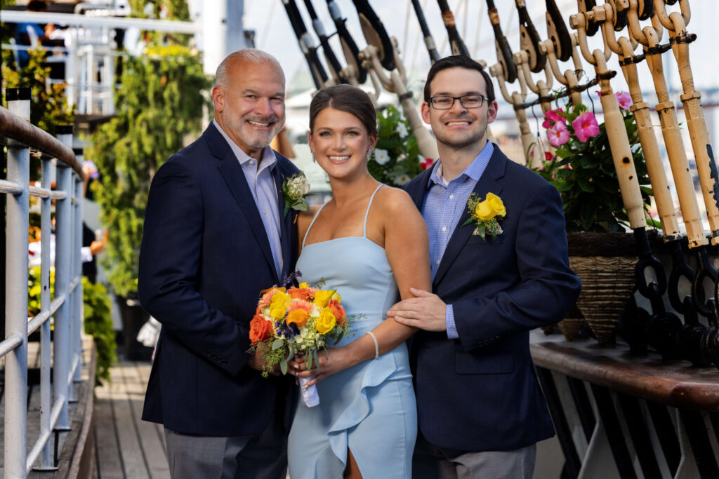 two men in blue suits posing with a woman in light blue dress at the moshulu in philadelphia