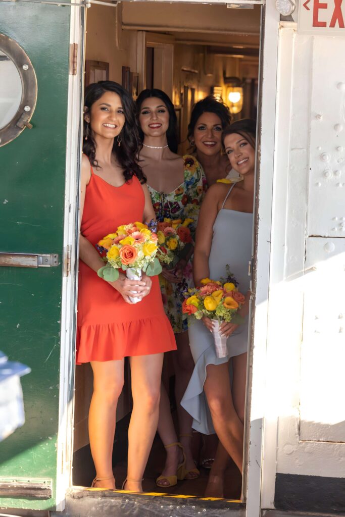 four women smiling and laughing with flower bouquets behind a ship door at the moshulu in philadelphia