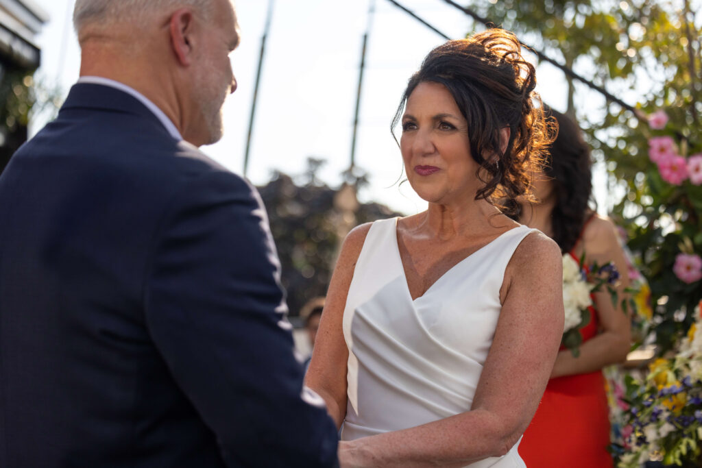 bride looking at groom as they stand together at floral altar and hold hands at the moshulu