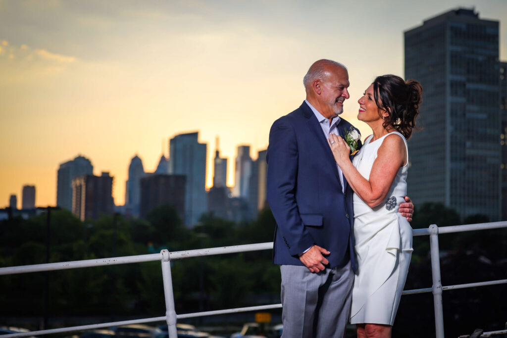 bride and groom sharing candid laughs with sunset skyline of philly in the background
