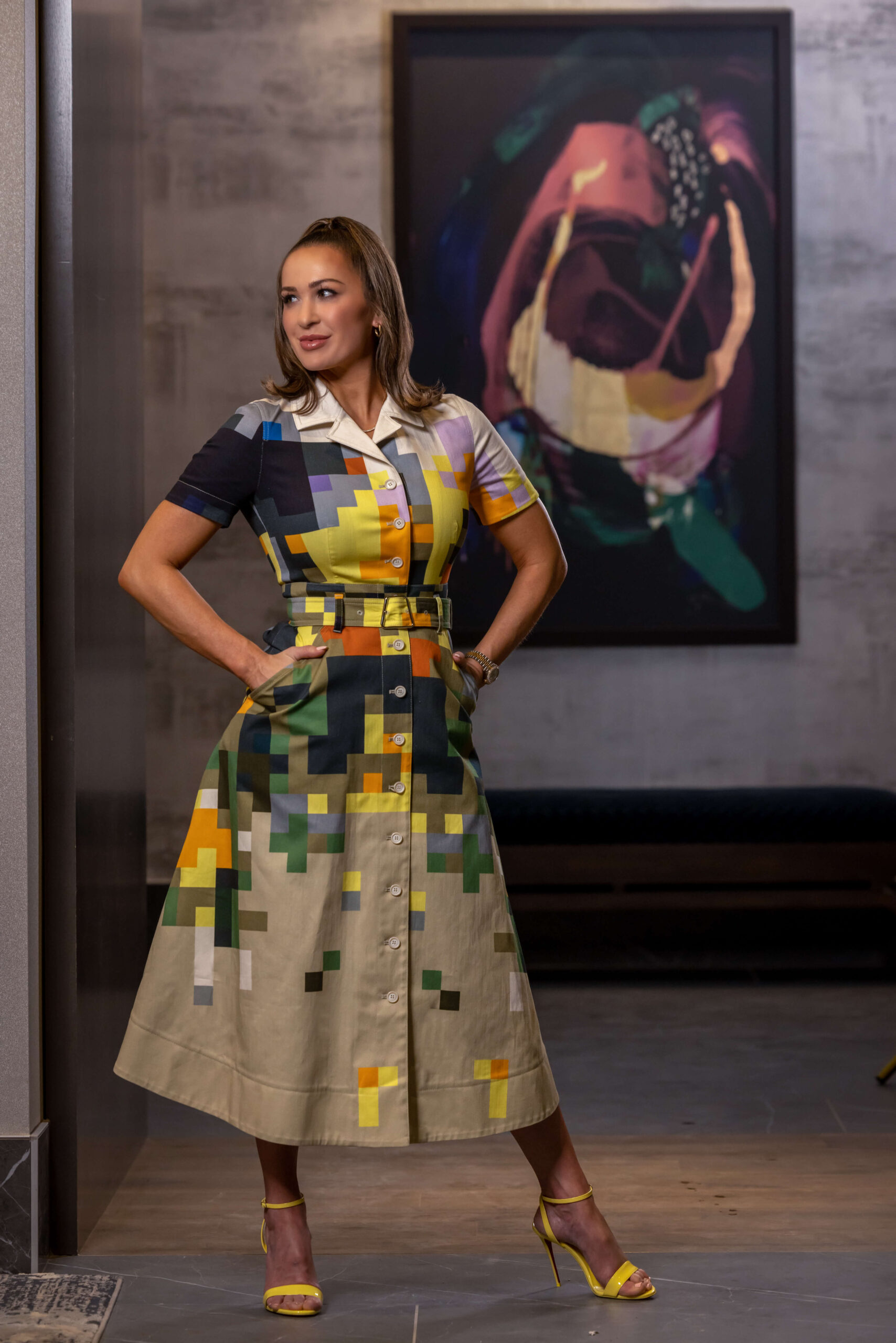 woman in stylish pixel dress posing with hands on hips against abstract art work on wall