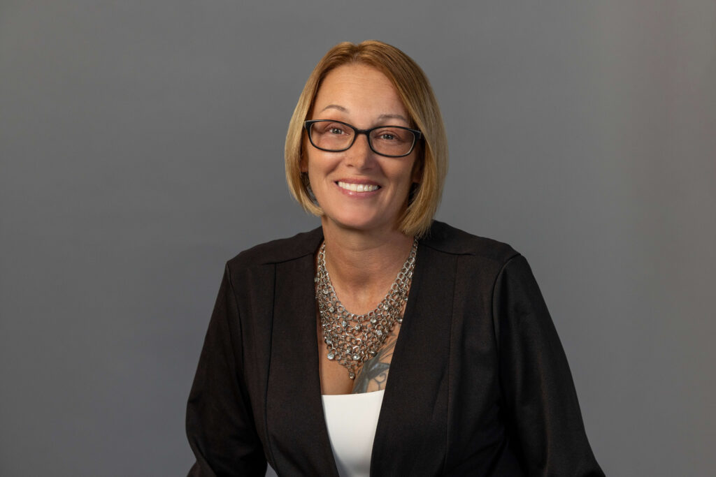 blonde woman smiling with glasses on against grey background