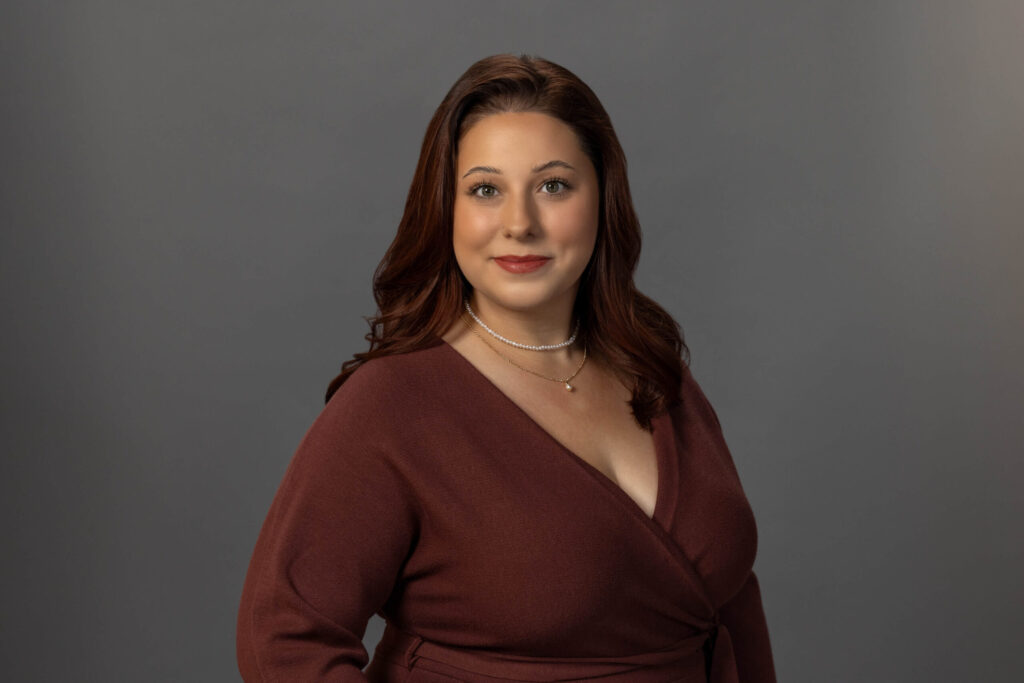 woman with slight smirk and burgundy dress poses in front of the camera