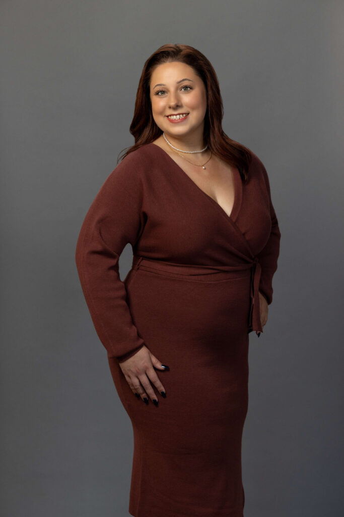woman strikes a pose in a burgundy dress and smiles wide for camera