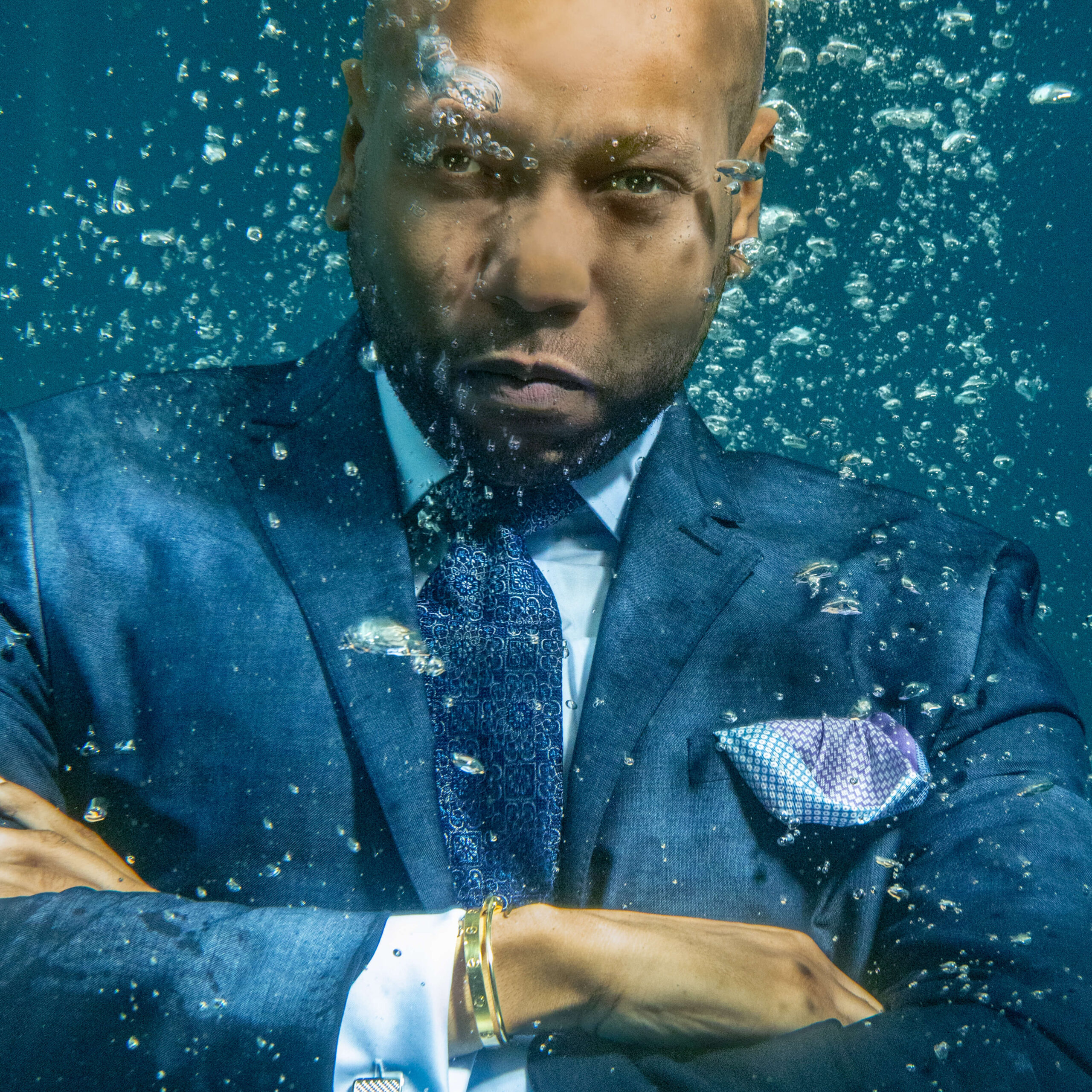 man crossing arms underwater in a luxury navy blue suit with a serious look on his face