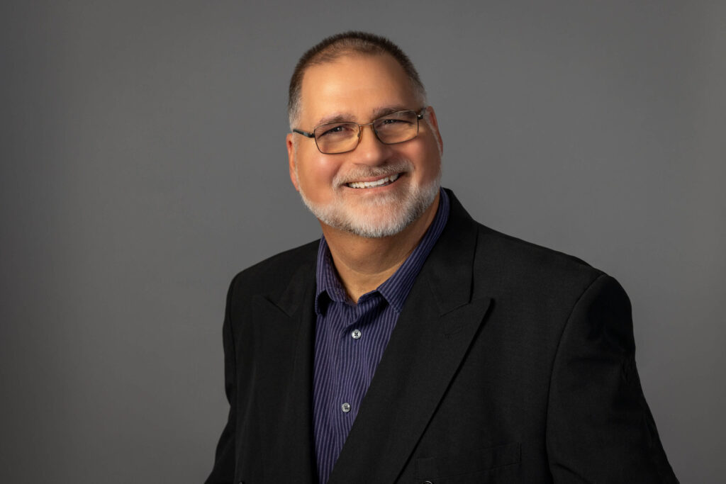 man smiling with glasses and black blazer on for studio portrait
