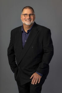 man poses with hand on leg against a grey background in a studio photo setting