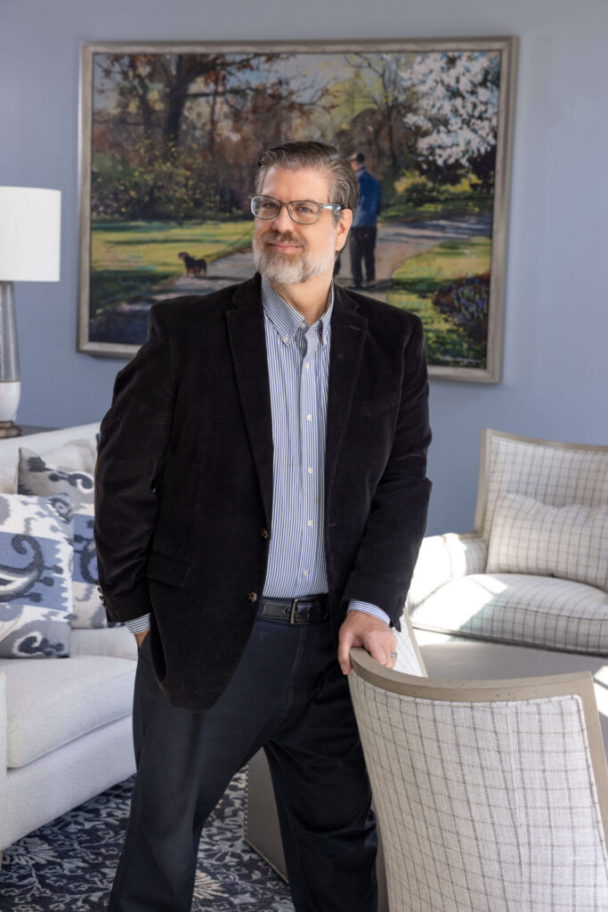 man looking off-camera while leaning against a chair in tidy living room space