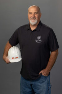 man in polo shirt and denim jeans holds a white construction helmet and smiles