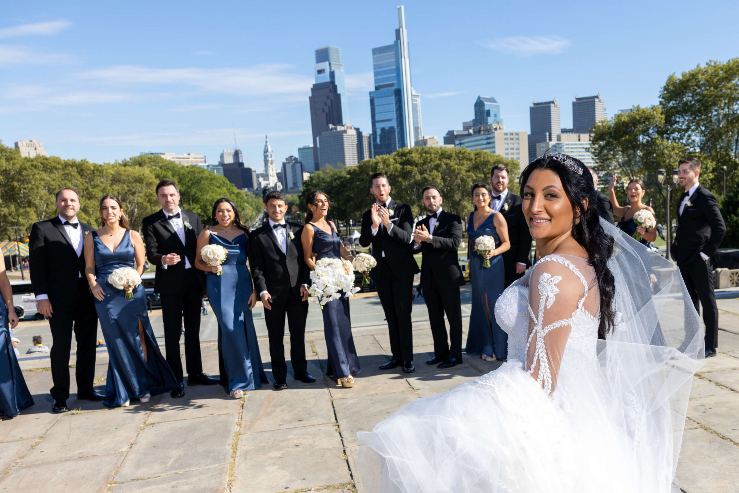 bride strikes a pose as she walks by wedding party at top of art museum steps in philly
