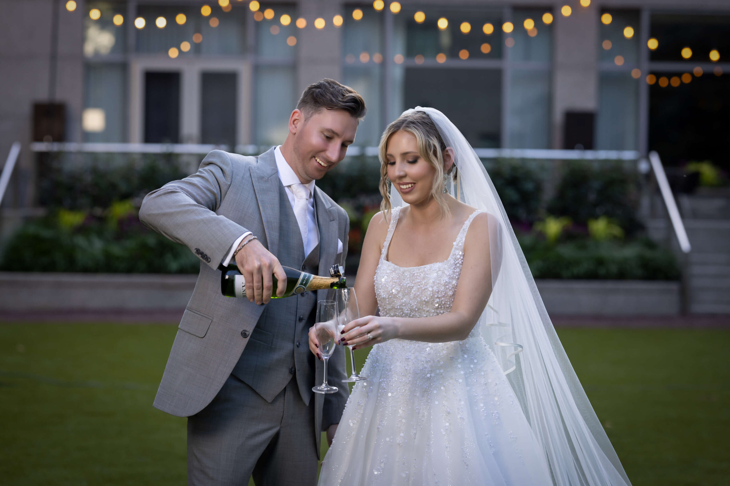groom pouring champagne into a glass while the bride holds it