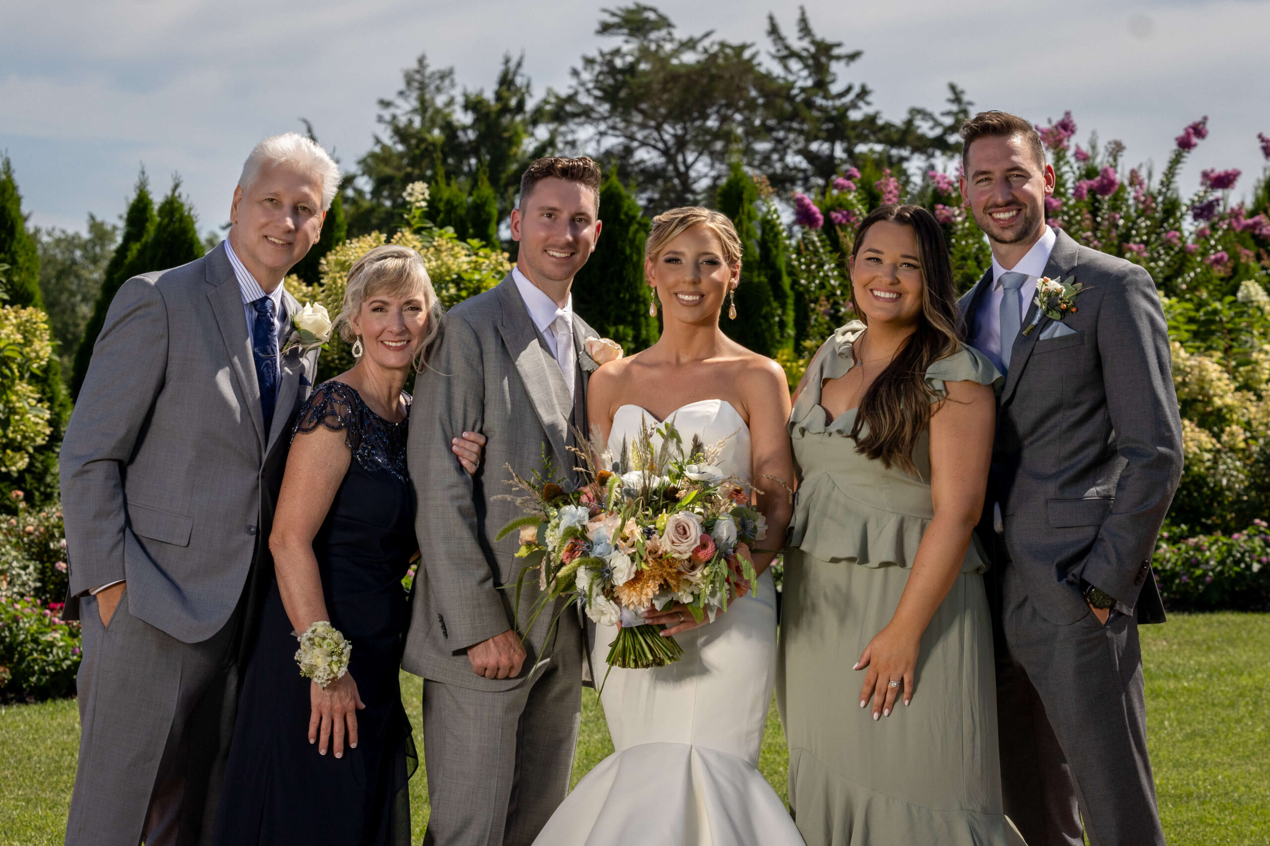 a bride and groom pose with their family at their outdoor wedding in a garden
