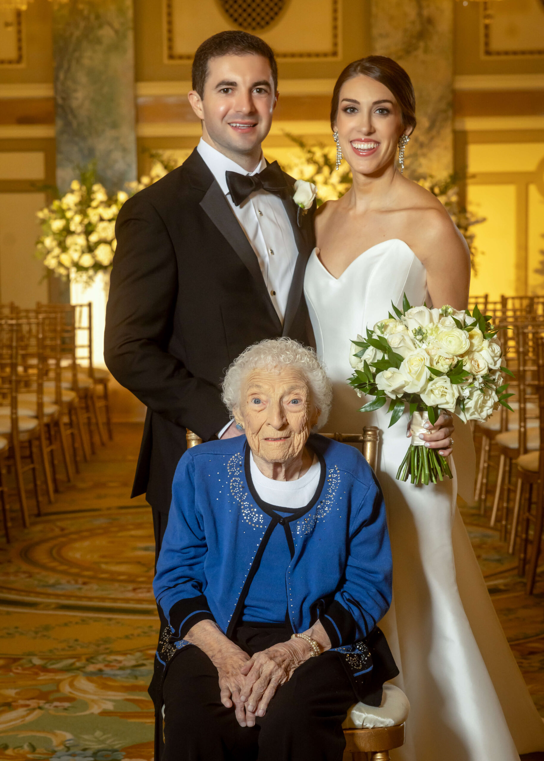a bride and groom pose for a photo with their grandmother in an extravagant ceremony room
