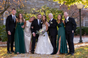 a bride and groom happily pose with their family members in front of a stone building