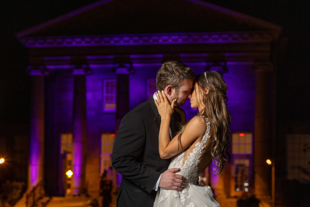 bride and groom kissing with purple lights shining on classic building