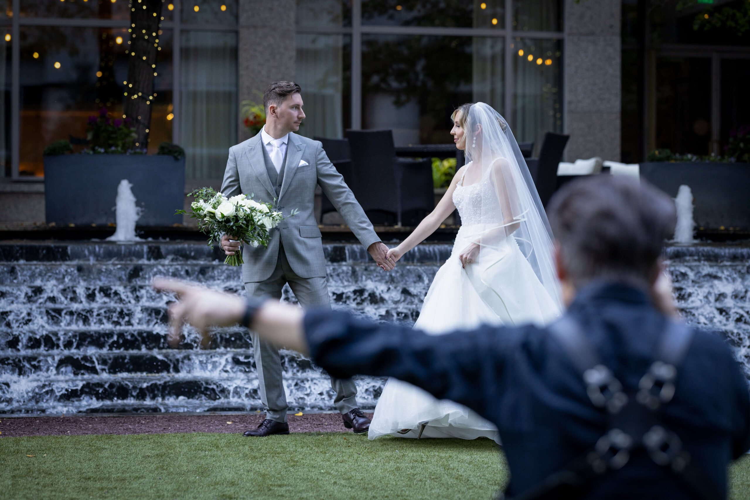 bride and groom walking in front of waterfall at the logan hotel in philly as wedding photographer gives direction