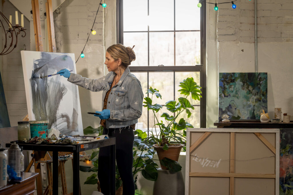 blonde woman painting with a brush in a rustic art studio