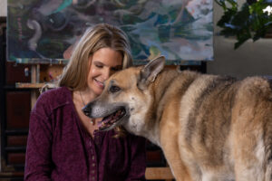 blonde woman posing with german shepherd dog against abstract art painting